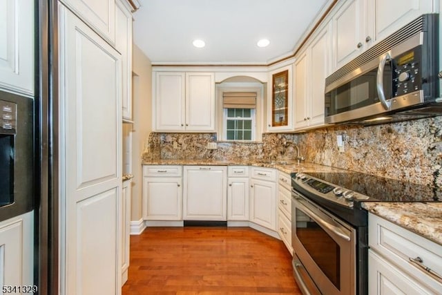 kitchen with decorative backsplash, appliances with stainless steel finishes, glass insert cabinets, light wood-style floors, and light stone countertops