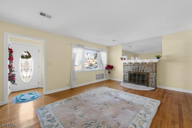 living room featuring a stone fireplace, wood finished floors, visible vents, and baseboards