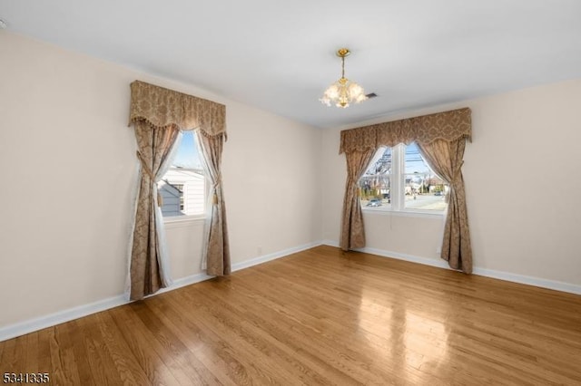 spare room featuring a chandelier, light wood-type flooring, and baseboards