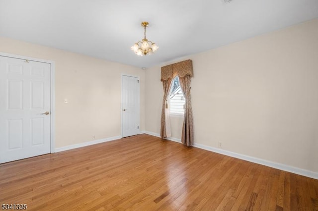 empty room featuring light wood-type flooring, baseboards, and a chandelier