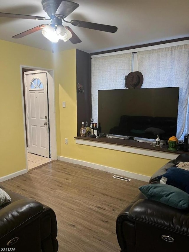 living room with ceiling fan, wood finished floors, visible vents, and baseboards