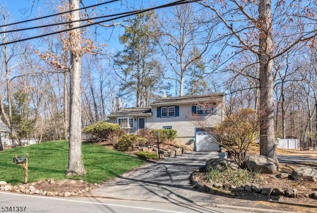 tri-level home with an attached garage, driveway, a chimney, and a front lawn