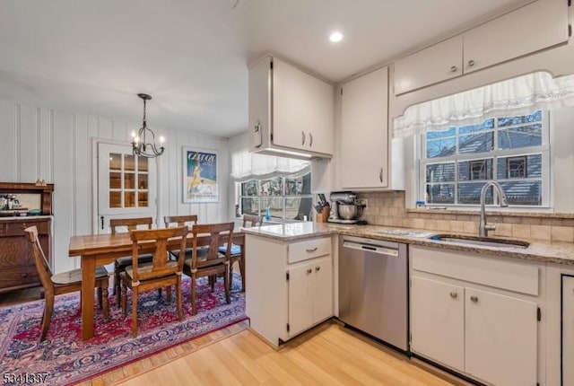 kitchen with a sink, white cabinets, stainless steel dishwasher, light wood-type flooring, and decorative backsplash