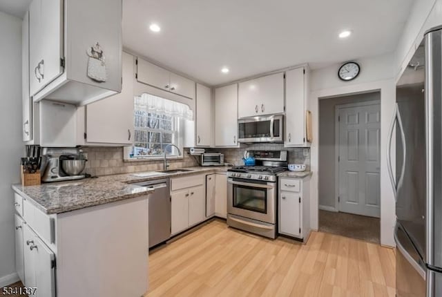 kitchen with appliances with stainless steel finishes, a sink, light wood-style flooring, and tasteful backsplash