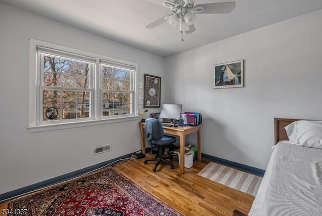 office with a ceiling fan, visible vents, baseboards, and wood finished floors