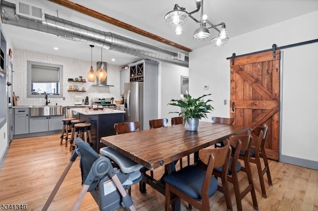 dining space featuring light wood finished floors, a barn door, and visible vents