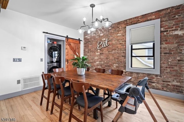 dining space featuring a barn door, visible vents, stacked washer and clothes dryer, brick wall, and light wood-style floors