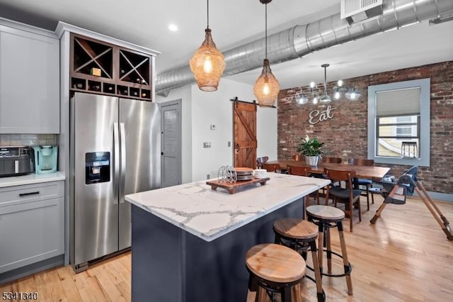 kitchen featuring a barn door, brick wall, a kitchen island, light wood-type flooring, and stainless steel fridge