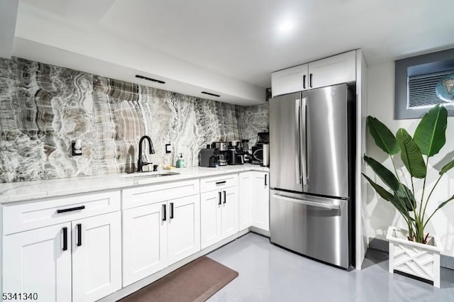 kitchen with finished concrete flooring, light stone counters, freestanding refrigerator, white cabinetry, and a sink