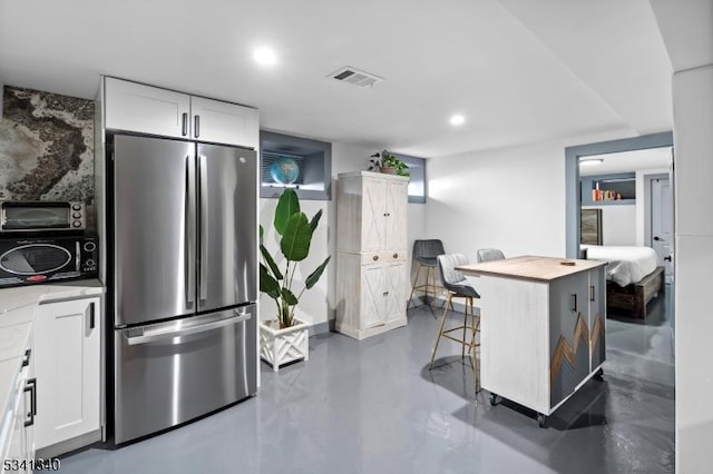 kitchen featuring visible vents, light countertops, freestanding refrigerator, and white cabinets