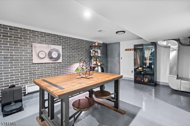 dining room with baseboards, finished concrete flooring, and brick wall