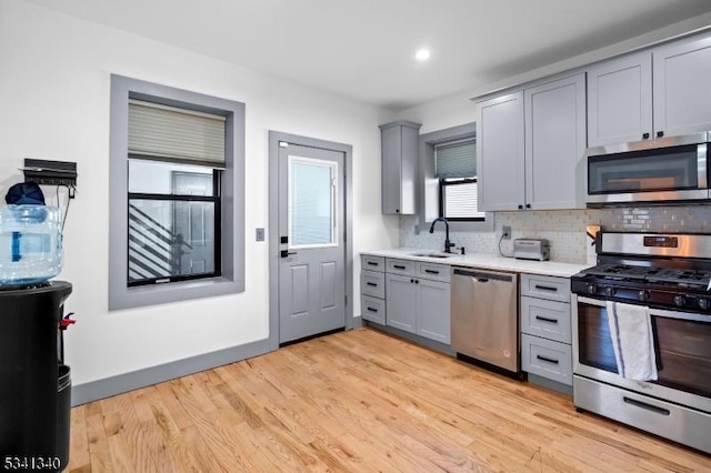 kitchen featuring stainless steel appliances, gray cabinets, light countertops, light wood-style floors, and a sink