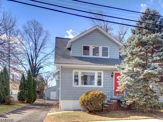 view of front facade featuring a shingled roof, entry steps, fence, and a garage