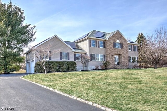 view of front facade with a garage, roof mounted solar panels, a front lawn, and driveway
