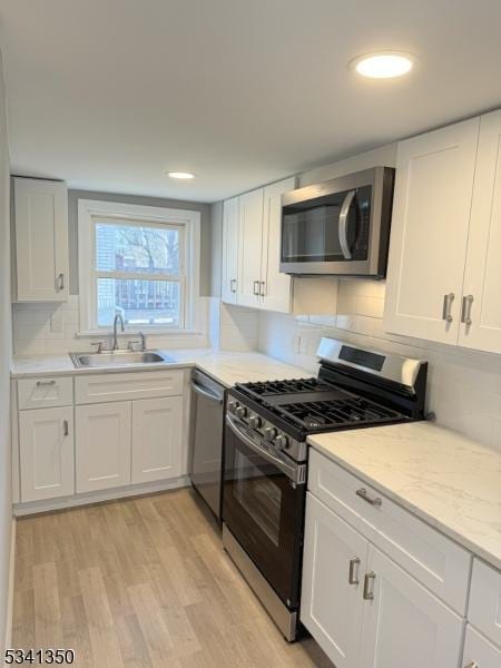 kitchen with appliances with stainless steel finishes, light wood-style floors, white cabinetry, and a sink