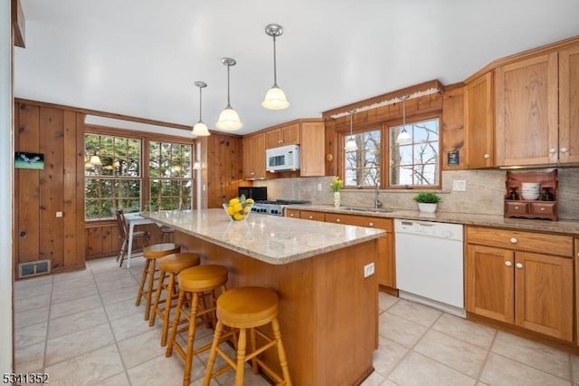 kitchen with tasteful backsplash, visible vents, a center island, white appliances, and a sink