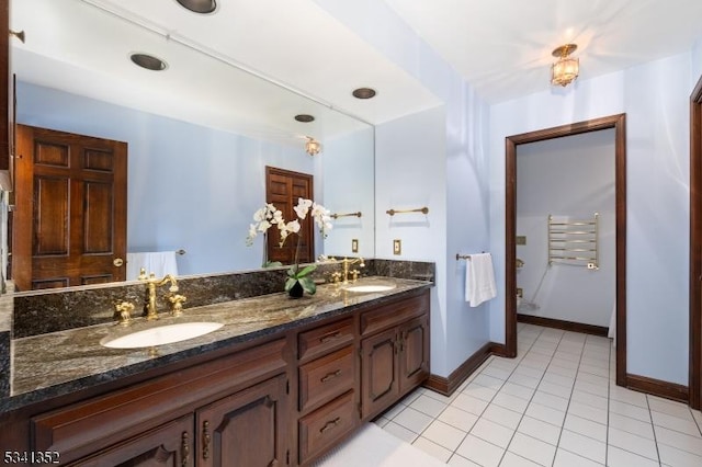 bathroom featuring tile patterned flooring, double vanity, baseboards, and a sink