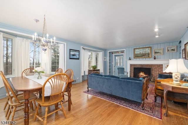 dining area featuring baseboards, light wood finished floors, an inviting chandelier, ornamental molding, and a brick fireplace