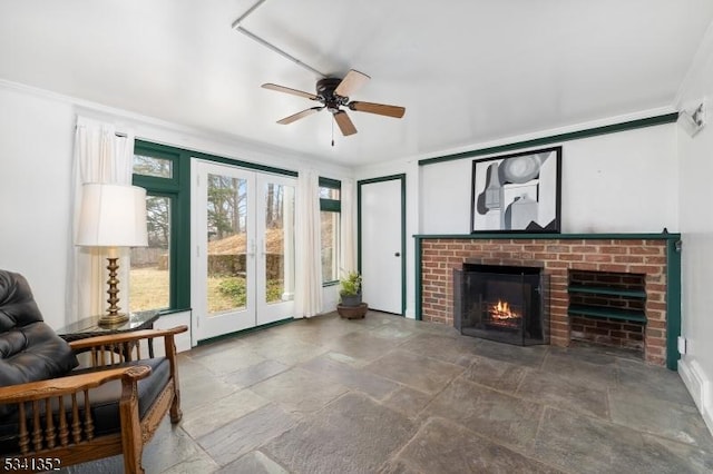 living area with a fireplace, ornamental molding, ceiling fan, stone finish floor, and french doors