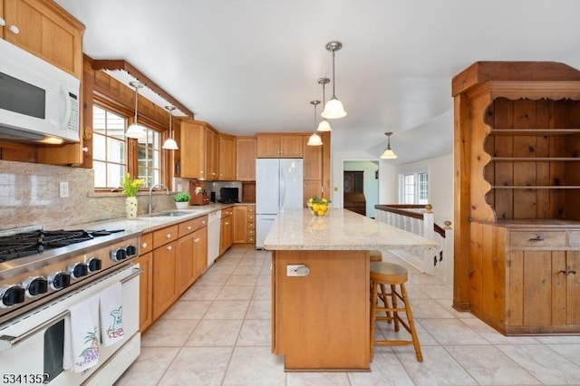 kitchen featuring white appliances, light stone countertops, a sink, decorative backsplash, and a center island