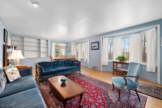 living room featuring visible vents, crown molding, baseboards, built in features, and wood finished floors