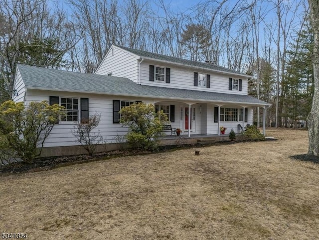 view of front of home with covered porch, a front yard, and roof with shingles