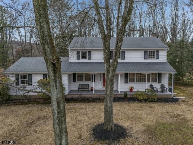 traditional home with a shingled roof, covered porch, and a chimney