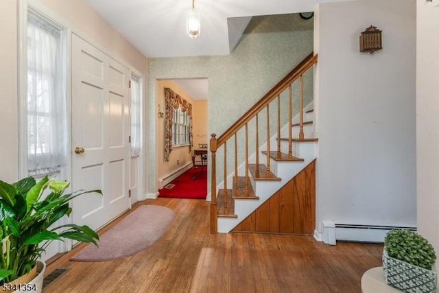 entrance foyer with wood-type flooring, visible vents, stairway, and baseboard heating