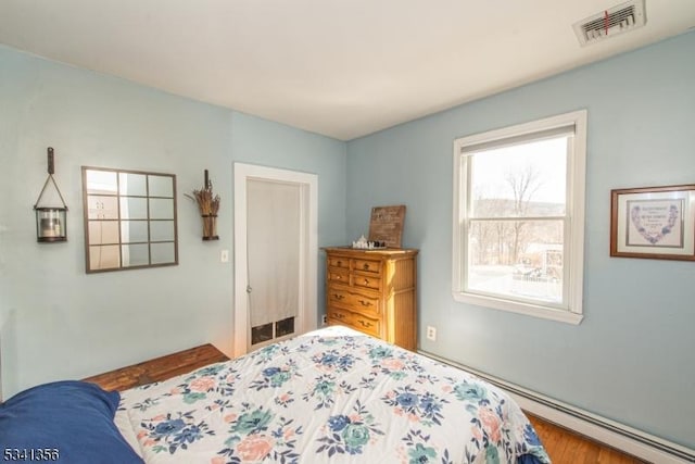 bedroom featuring a baseboard radiator, visible vents, and wood finished floors