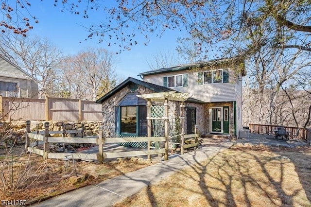 view of front of house featuring stone siding, fence, and a patio