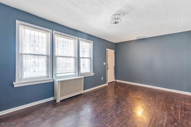 empty room with radiator heating unit, baseboards, and wood finished floors