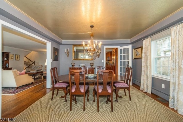 dining room with a notable chandelier, wood finished floors, ornamental molding, baseboard heating, and stairway