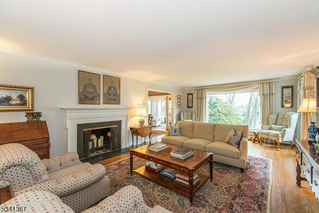 living area featuring a fireplace with flush hearth, wood finished floors, and crown molding