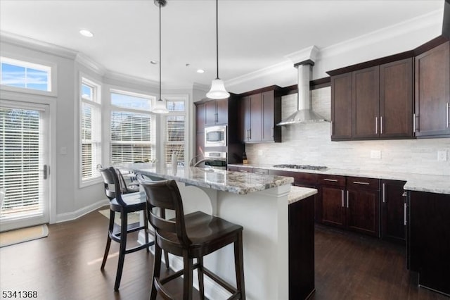 kitchen featuring a kitchen breakfast bar, ornamental molding, appliances with stainless steel finishes, wall chimney range hood, and dark wood-style floors