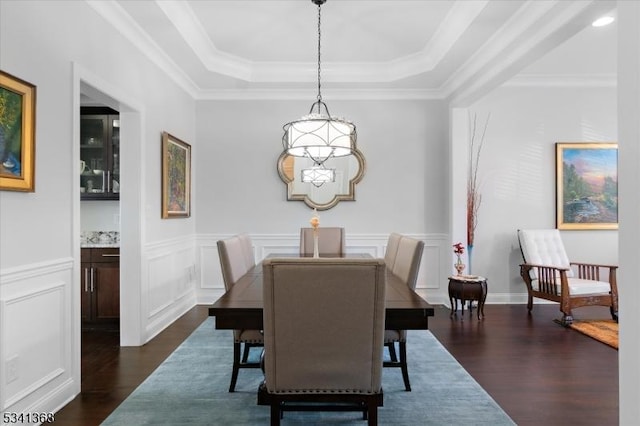 dining room with a decorative wall, a wainscoted wall, dark wood-type flooring, ornamental molding, and a raised ceiling