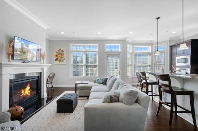 living room featuring baseboards, a glass covered fireplace, dark wood-style flooring, crown molding, and recessed lighting