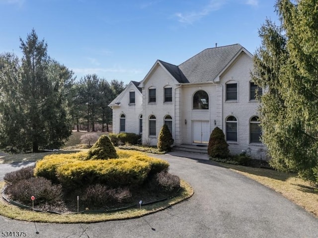 french provincial home featuring driveway, roof with shingles, and brick siding