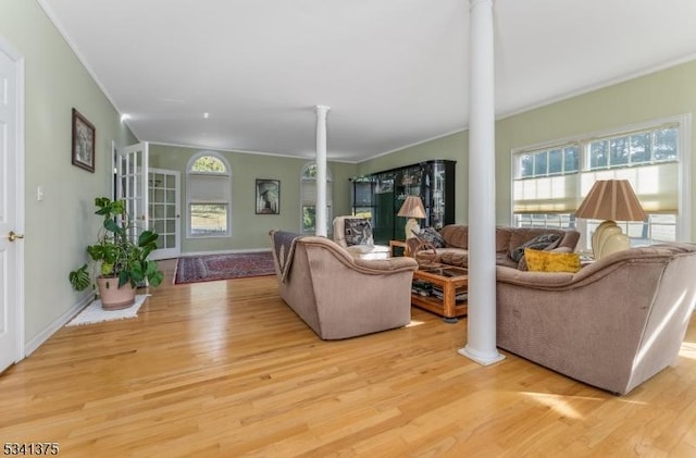 living area with crown molding, light wood finished floors, baseboards, and ornate columns