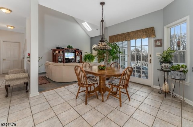 dining space with lofted ceiling with skylight, baseboards, and light tile patterned floors