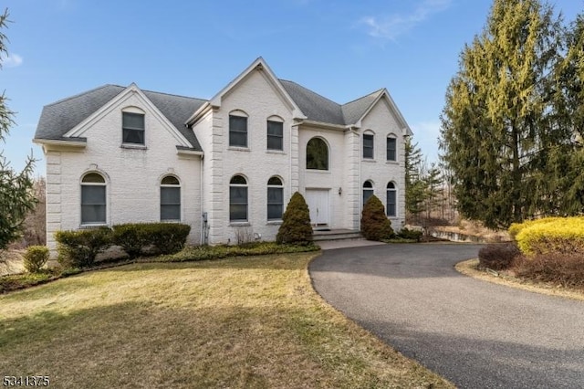 french provincial home with brick siding, roof with shingles, a front yard, and aphalt driveway