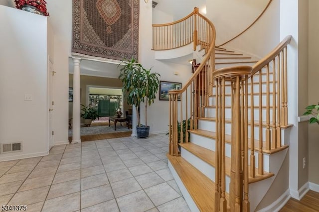 staircase featuring a towering ceiling, visible vents, baseboards, tile patterned floors, and decorative columns