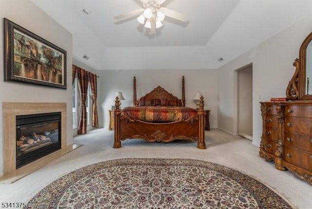 bedroom featuring a tray ceiling, a glass covered fireplace, and carpet