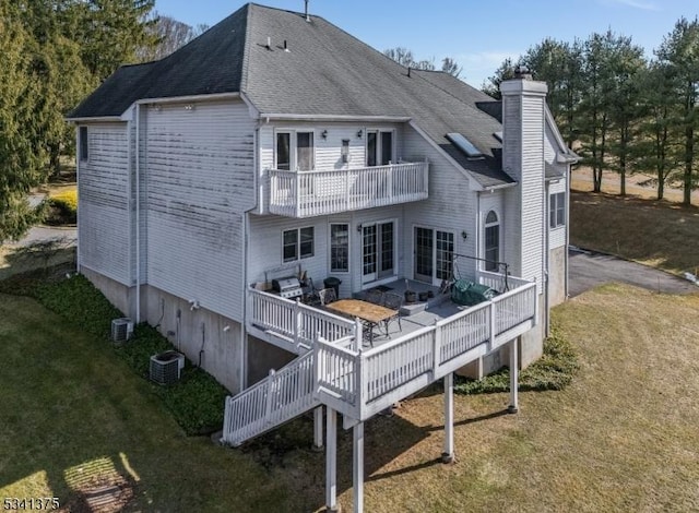 rear view of house with a balcony, a chimney, central AC, and a lawn