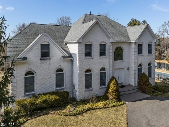 french country style house with roof with shingles and brick siding