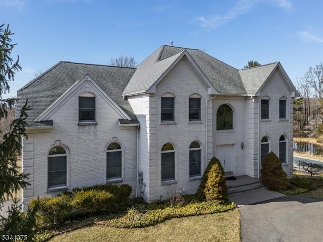 french country inspired facade featuring brick siding and a shingled roof