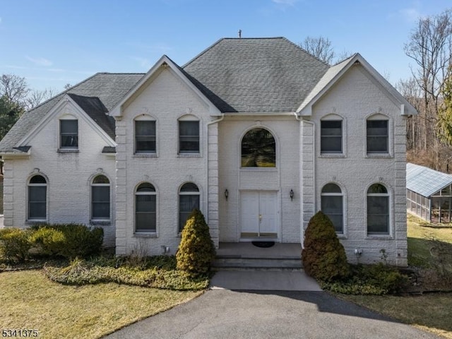 french provincial home featuring a front yard, brick siding, and roof with shingles