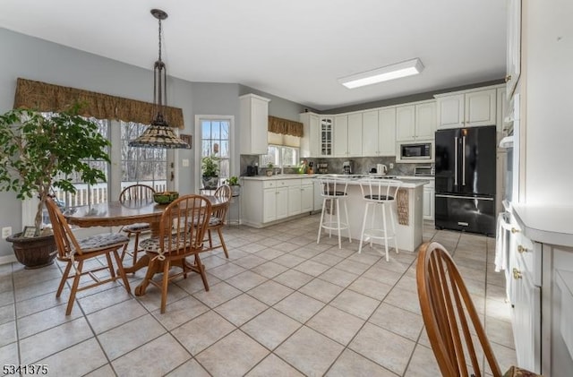 kitchen with light tile patterned floors, a kitchen island, freestanding refrigerator, built in microwave, and light countertops