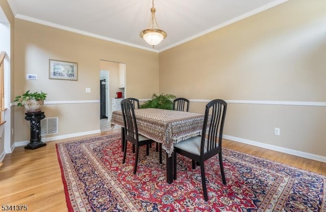 dining space with baseboards, light wood-type flooring, visible vents, and crown molding