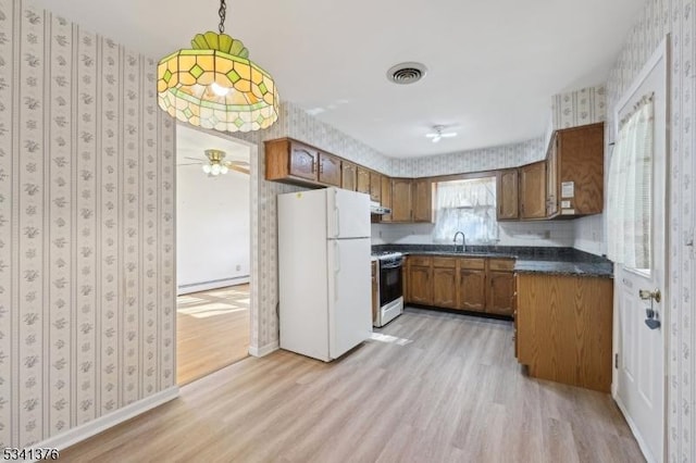 kitchen with dark countertops, wallpapered walls, range with gas stovetop, freestanding refrigerator, and brown cabinetry