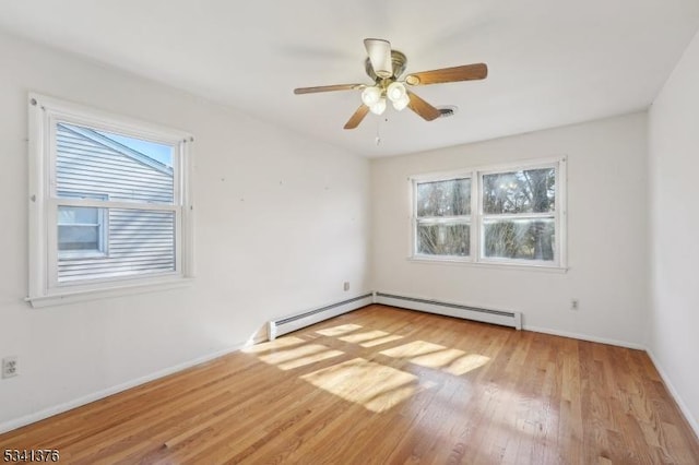 unfurnished room with plenty of natural light, a baseboard heating unit, baseboards, and wood finished floors